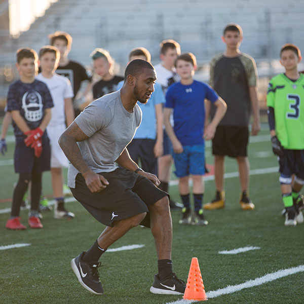 Coach Javes Lewis demonstrating a cutting drill around a cone as young players watch