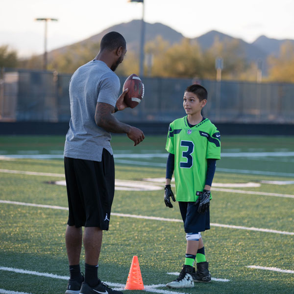 Coach giving one-on-one instruction to a young player holding a football